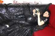 Lucy wearing a supersexy black rain catsuit posing and lolling on a sofa (Pics)