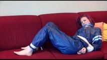 Mara tied and gagged on a sofa wearing a shiny blue PVC sauna suit (Video)