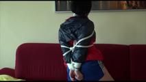 Jill tied and gagged on a sofa wearing a sexy blue shiny nylon shorts and a red/blue oldschool rain jacket (Video)