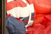 Mara tied, gagged and hooded on bed wearing a shiny red/blue/white striped old school down jacket and a skibib in red (Pics)