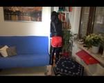 Mara wearing a red shiny nylon shorts over a black rainpants and a rain jacket while searching a book and lolling on the sofa (Video)