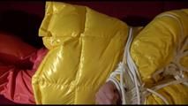 Lucy tied, gagged and hooded on a red sofa wearing an orange venice beach pant and a yellow down jacket (Video)