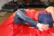 Sonja tied and gagged with ropes and cloth gag on a bed wearing a sexy oldschool darkblue shiny nylon shorts and red/blue rain jacket (Pics)