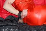 Pia tied and gagged with nack ties on a bed wearing a sexy red shiny nylon rainwear catsuit (Pics)