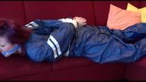 Mara tied and gagged on a sofa wearing a shiny blue PVC sauna suit (Video)