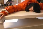 Mara tied and gagged on a table wearing a sexy black down pants and an orange down jacket (Pics)