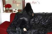 Lucy wearing a supersexy black rain catsuit posing and lolling on a sofa (Pics)