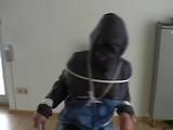 An archive girl tied, gagged and hooded two times on a sofa and chair wearing a shiny blue rainwear (Video)