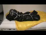 Jill in a blue shiny down jacket and black shiny rainwear tied and gagged in a shiny red/black big shiny nylon bag to lie in (Video)