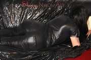 Lucy wearing a supersexy black rain catsuit posing and lolling on a sofa (Pics)