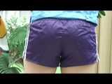 Watching our sexy archive girl wearing a purple shiny nylon shorts and a lightblue rainjacket being at home (Video)