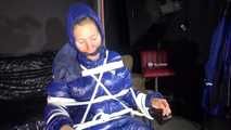 Watching sexy Sandra wearing a sexy blue shiny nylon rainpants and a blue down jacket being tied and gagged and hooded with ropes on a hairdressers chair covered with a rain cape (Video)