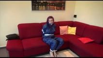 Mara tied and gagged on a sofa wearing a shiny blue PVC sauna suit (Video)