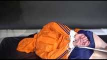 Lucy tied and gagged on a bed wearing a blue shiny nylon shorts and an orange shiny nylon rain jacket (Video)