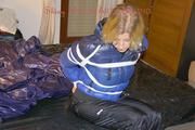 Pia tied, gagged and hooded on a bed wearing a sexy black shiny nylon pants and a blue/black down jacket (Pics)