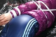 Mara tied and gagged on bed wearing a shiny purple down jacket and a blue rain pants (Pics)