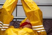 Pia tied and gagged in bed in a yellow rainsuit and a red gag