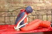 Mara tied, gagged and hooded on bed wearing a shiny red/blue/white striped old school down jacket and a skibib in red (Pics)