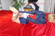 Sonja tied and gagged with ropes and cloth gag on a bed wearing a sexy oldschool darkblue shiny nylon shorts and red/blue rain jacket (Pics)