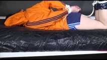 Lucy tied and gagged on a bed wearing a blue shiny nylon shorts and an orange shiny nylon rain jacket (Video)