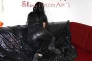 Lucy wearing a supersexy black rain catsuit posing and lolling on a sofa (Pics)