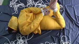Archive girl tied and gagged on bed wearing a shiny yellow rainwear (Video)