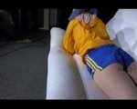 SEXY Mara wearing a blue shiny nylon shorts and a yellow rain jacket reading and lolling on the sofa (Video)
