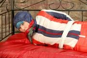 Mara tied, gagged and hooded on bed wearing a shiny red/blue/white striped old school down jacket and a skibib in red (Pics)