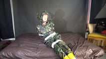 Watching sexy Pia being tied and gagged with tape on a bed wearing a sexy camouflage shiny nylon rainpants and a rainjacket as well as yellow rubber boots (Video)