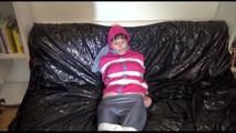 Mara tied and gagged with tape on a blue sofa wearing a supersexy pink/grey rainwear combination (Video)