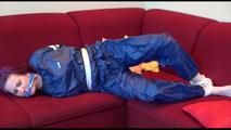 Mara tied and gagged on a sofa wearing a shiny blue PVC sauna suit (Video)
