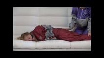 Sophie tied and gagged by Jill on a sofa wearing a shiny silver PVC sauna suit which is slitted by Jill (Video)