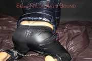 Sexy Sandra wearing a sexy shiny black rain pants and a sexy black down jacket with coat ties, gagges and hoodes herself on a bed with shiny nylon linen (Pics)