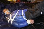 Pia tied, gagged and hooded on a bed wearing a sexy black shiny nylon pants and a blue/black down jacket (Pics)