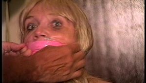50 Yr OLD REAL ESTATE AGENT IS NUDE, TIT TIED, CROTCH ROPED, WRAP BONDAGE TAPE GAGGED, CLEAR TAPE GAGGED AND  HANDGAGGED WHILE TIED TO A CHAIR (D71-15)