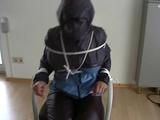 An archive girl tied, gagged and hooded two times on a sofa and chair wearing a shiny blue rainwear (Video)