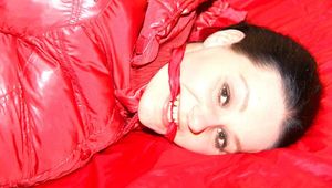 Lucy tied, gagged and hooded on a bed wearing a sexy black shiny nylon pants and a red down jacket (Pics)